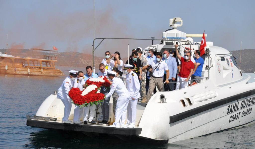 Boats adorned with Turkish flags celebrating the maritime festival, accompanied by a water-spraying tugboat.
