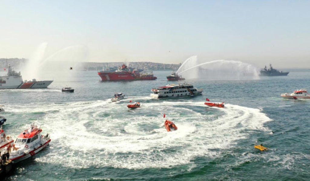 Boats adorned with Turkish flags celebrating the maritime festival, accompanied by a water-spraying tugboat.